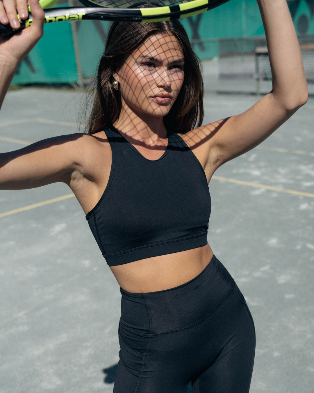 Woman posing on tennis court wearing sports bra and biker shorts