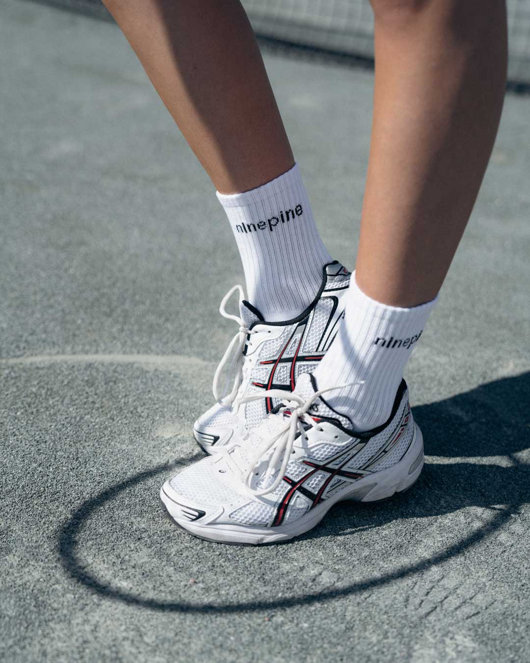 Close up of ninepine white socks and asics tennis shoes on tennis court