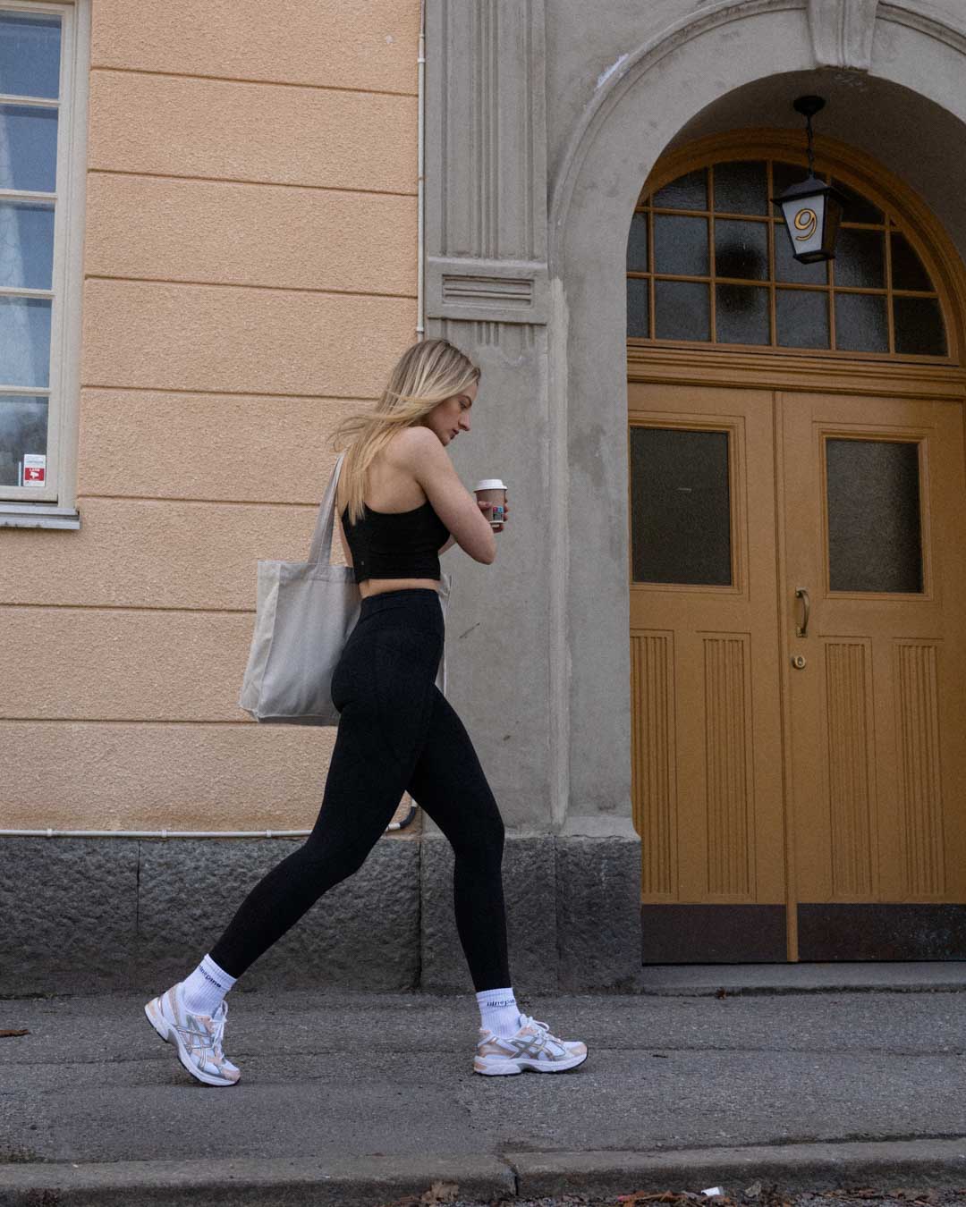 Blonde woman in sports leggings and sports bra walking down a Stockholm street