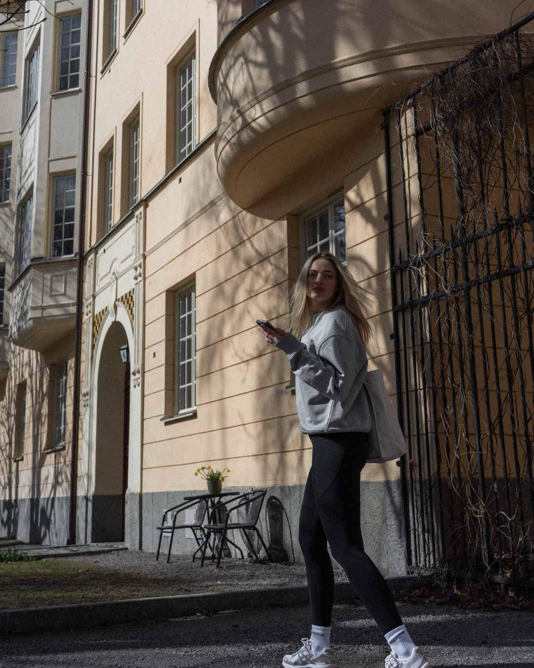 Woman in ninepine leggings and oversized sweatshirt in front of a historic European apartment complex