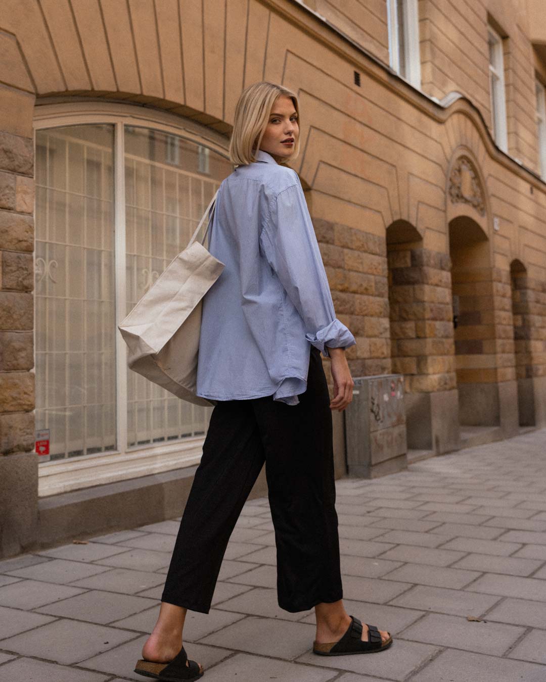 Blonde woman in cropped ninepine pants and blue shirt walking down a Stockholm street