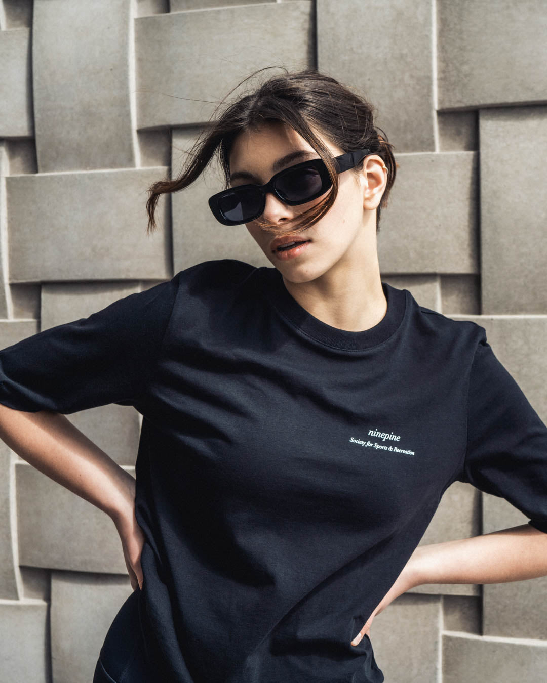 Woman posing in a ninepine black t-shirt with rectangular sunglasses