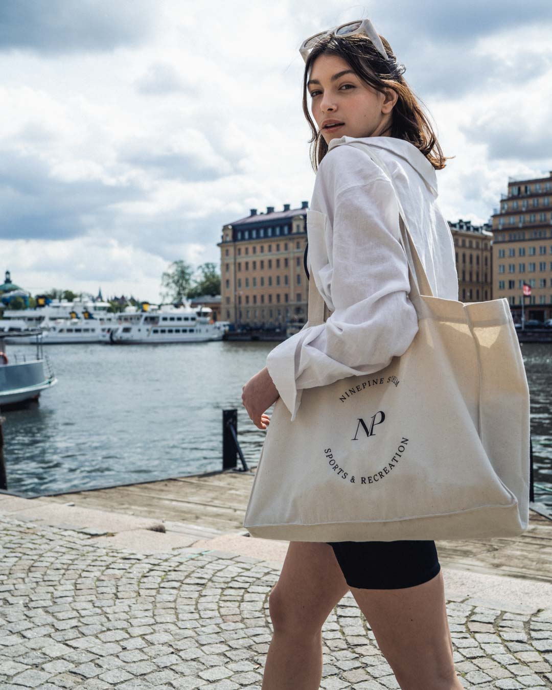 Woman walking by the water in biker shorts and a ninepine canvas tote bag