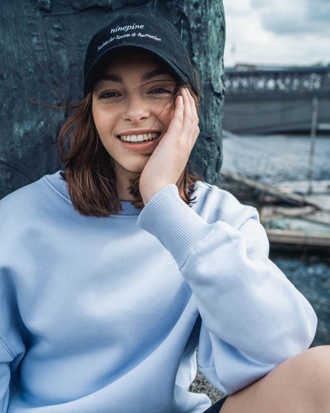 Woman in a blue ninepine sweatshirt and black cap smiling