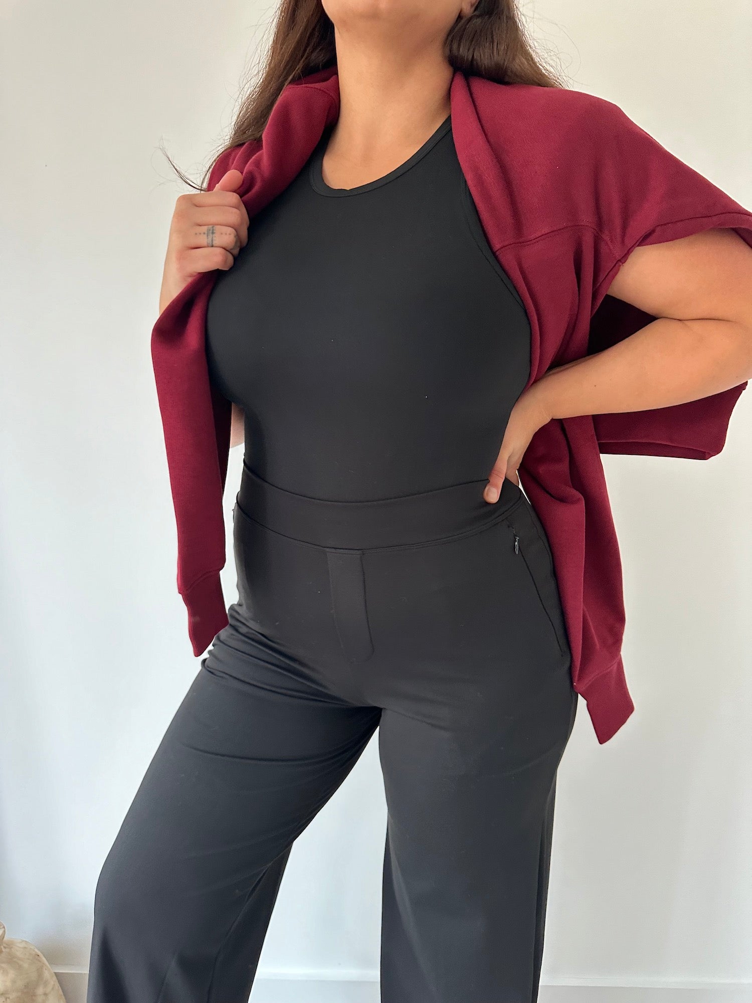 Eine kurvige Frau in einer schwarzen Ninepine Asana Relaxed-Hose, kombiniert mit einem weichen Oberteil und einem burgunderroten Pullover – ein Outfit, das die bequeme Stretchhose für den Alltag perfekt zur Geltung bringt