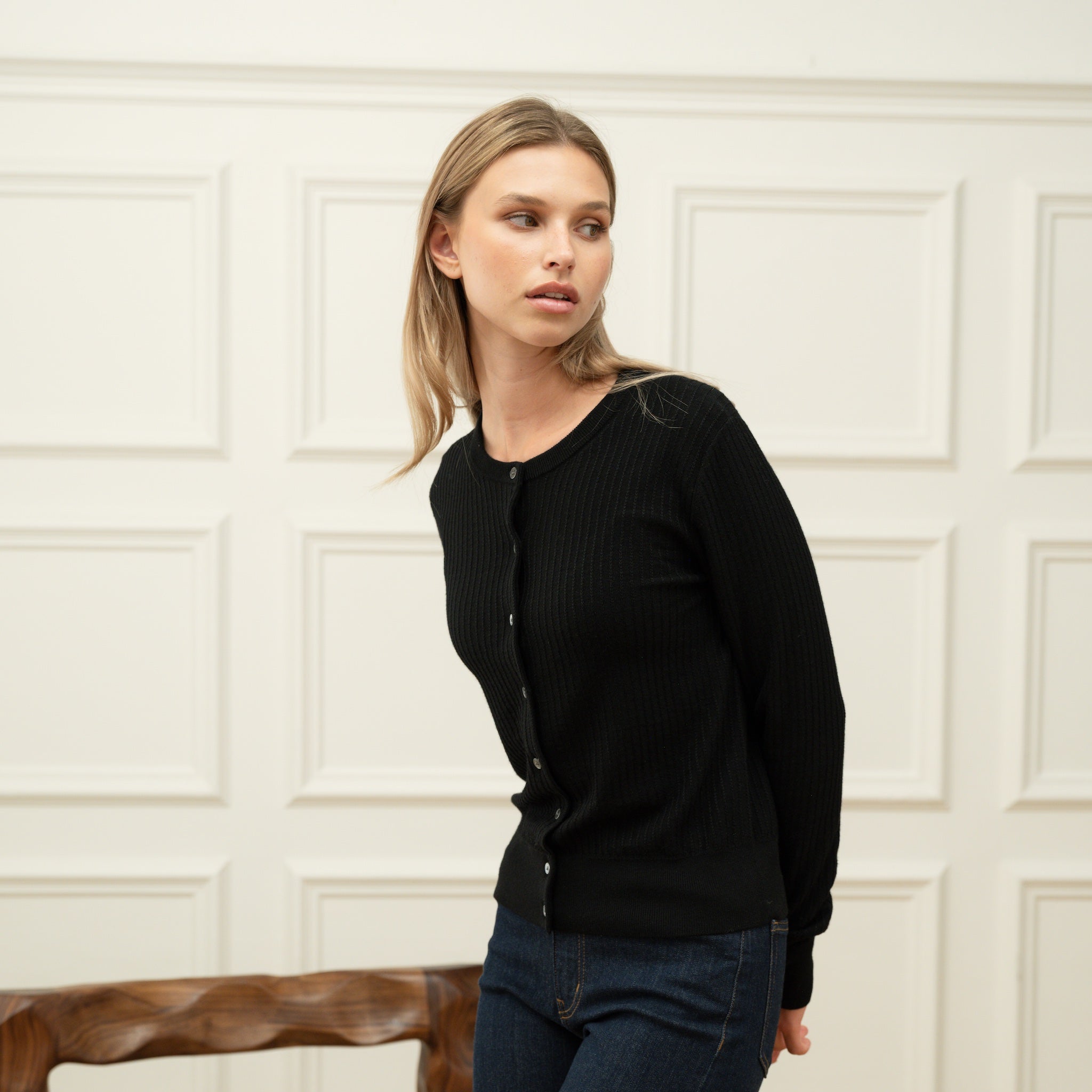Woman wearing a Ninepine black merino wool cardigan buttoned up against an off-white wall