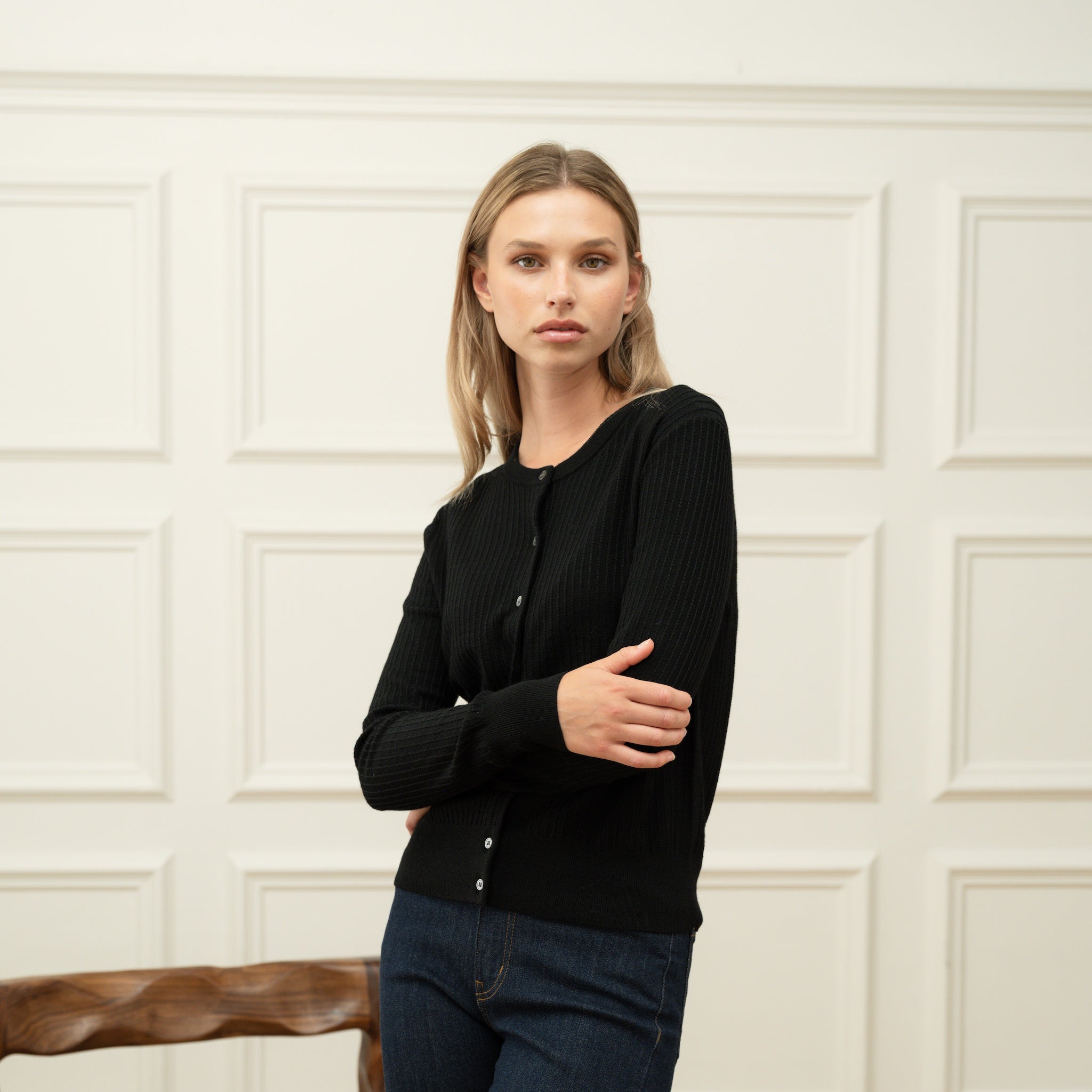 Woman wearing a Ninepine black merino wool cardigan in a bright minimalist interior