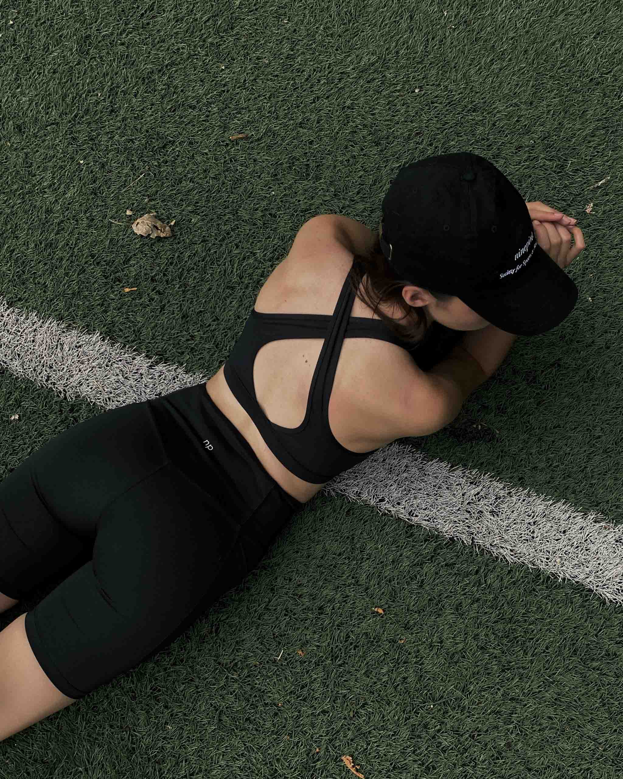 Girl in ninepine cap, ninepine biker shorts and bra lying on synthetic grass