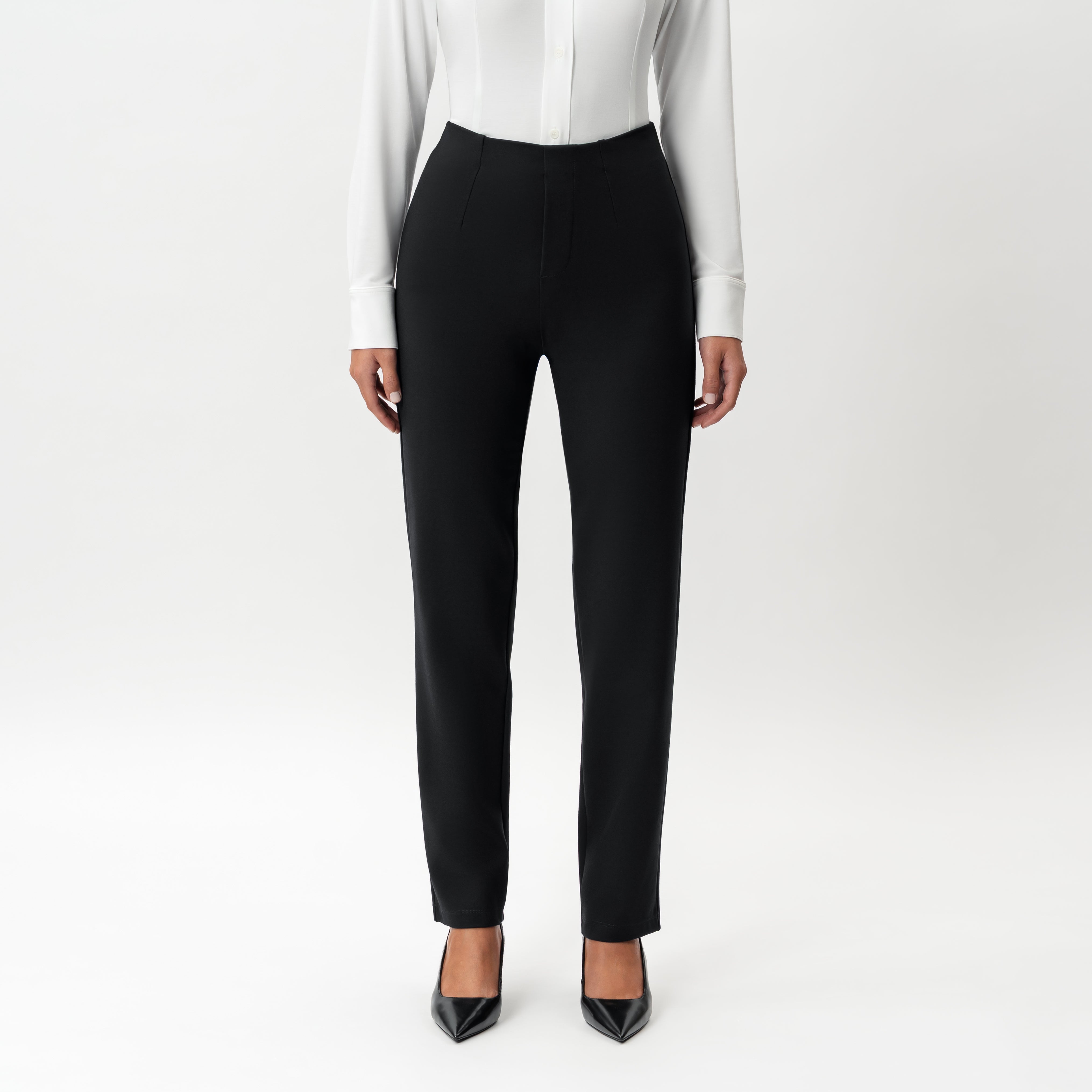Front view of model wearing black Ninepine Tailored Ponte Straight Trousers with a white shirt and black heels.