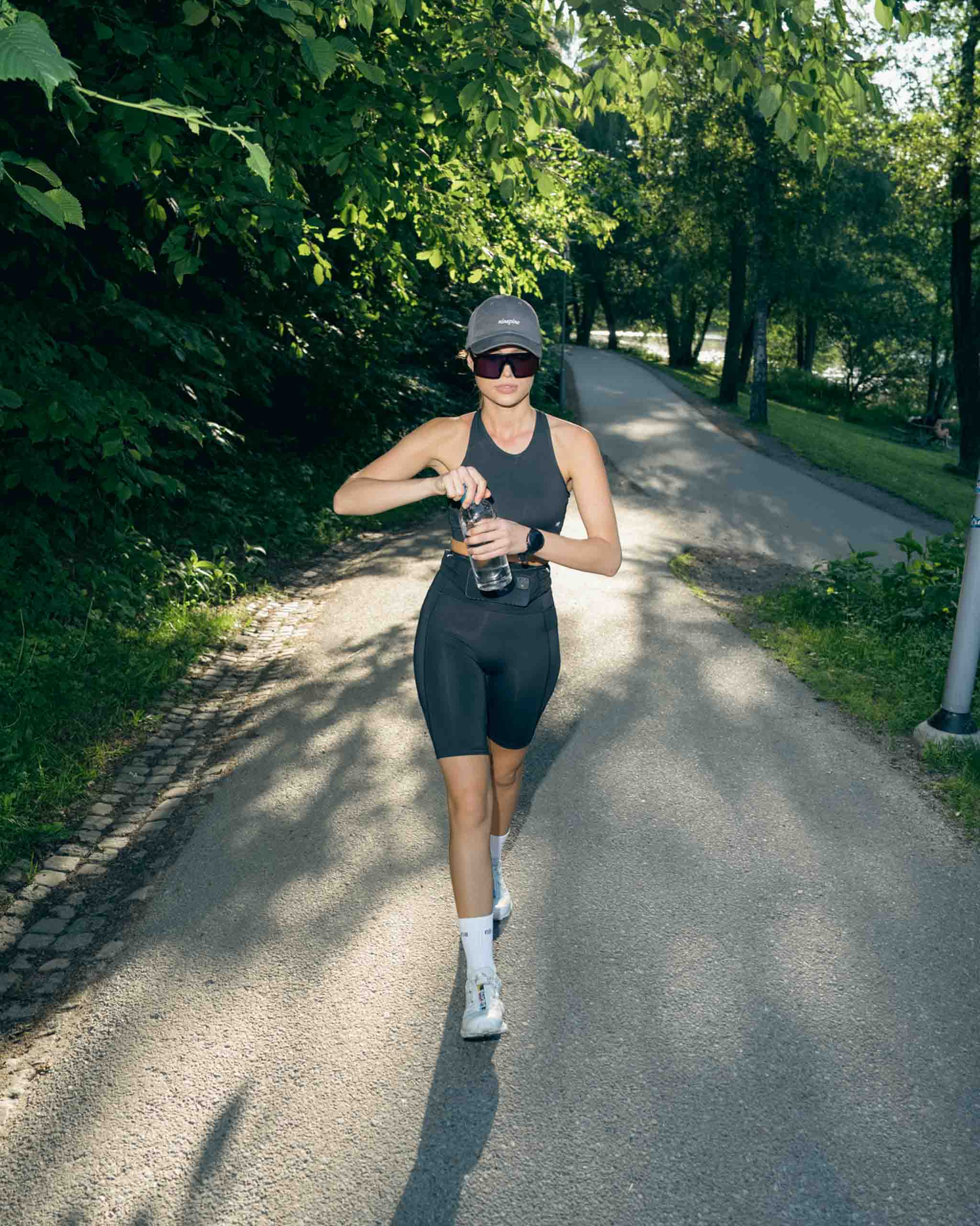 Mädchen läuft in Ninepine-Sportbekleidung mit einer Wasserflasche in der Hand durch einen Park.