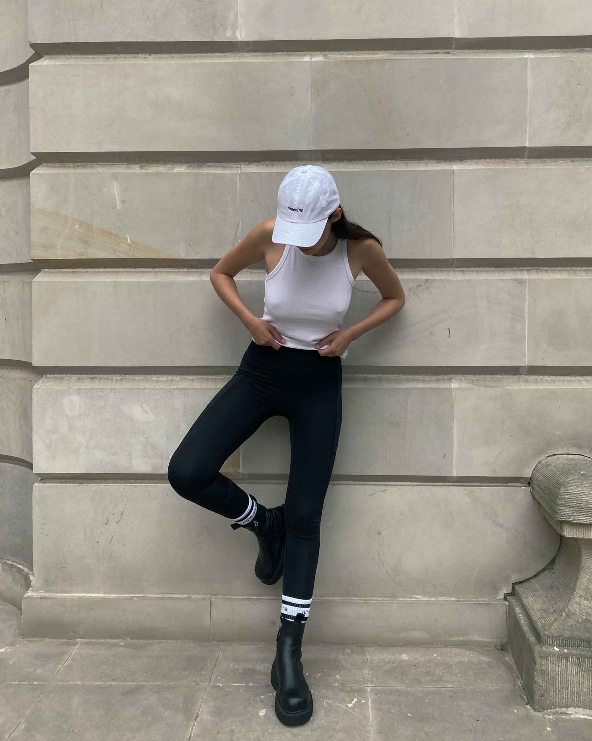 Mädchen posiert auf Sandsteinmauer mit Ninepine-Mütze und Ninepine-Leggings